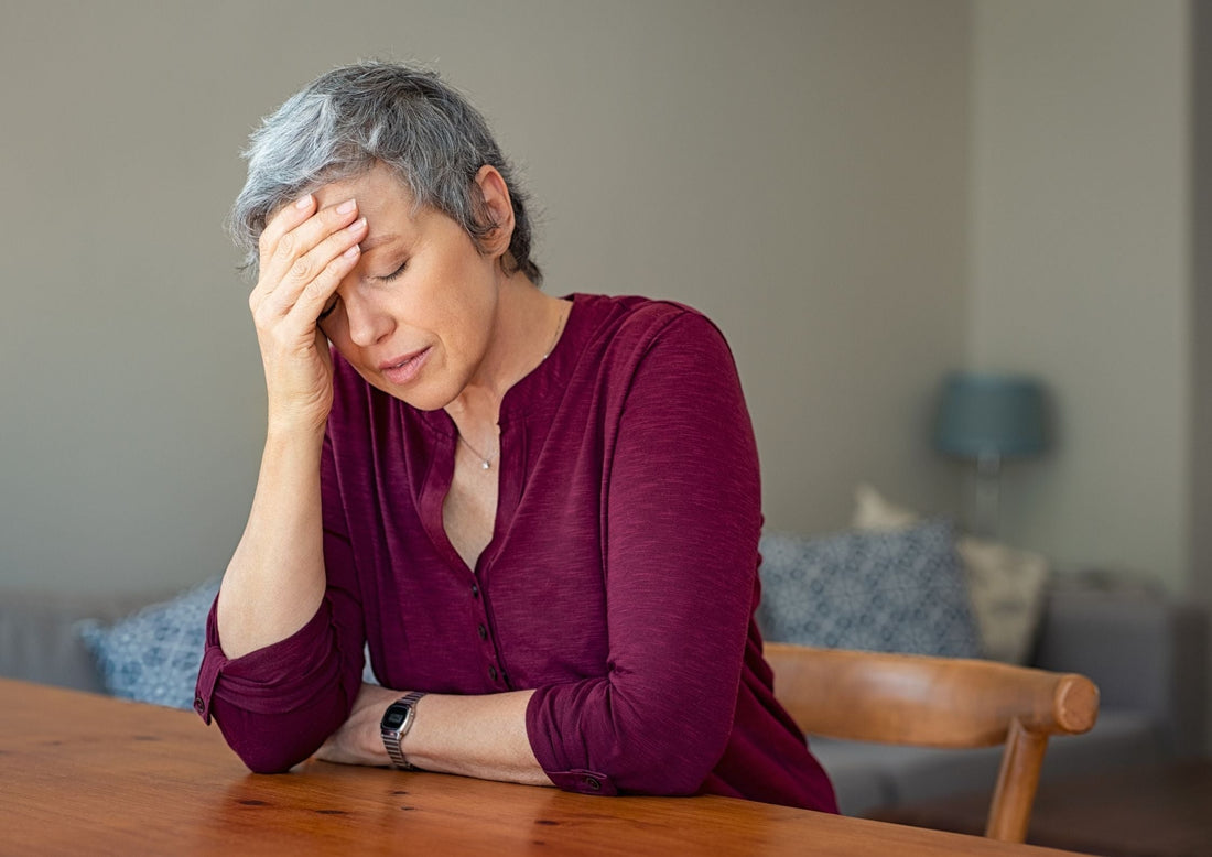 Tired middle-aged woman resting her forehead on her hand at a kitchen table